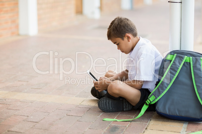 Schoolboy sitting in corridor and using digital tablet