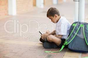 Schoolboy sitting in corridor and using digital tablet