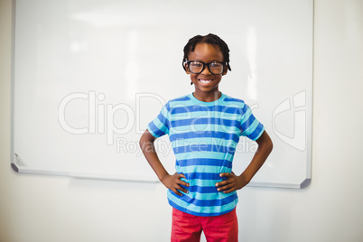 Happy schoolboy smiling in classroom with hand on hip