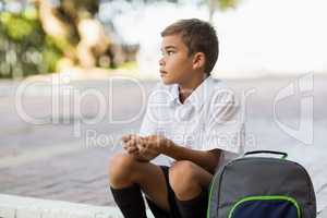 Thoughtful schoolboy sitting alone in campus