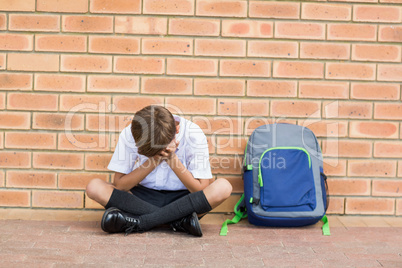 Sad schoolboy sitting alone in corridor