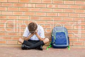 Sad schoolboy sitting alone in corridor