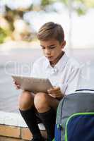 Schoolboy sitting in campus and using digital tablet