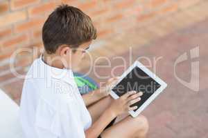Schoolboy sitting in corridor and using digital tablet