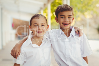 Smiling school kids standing with arm around in corridor