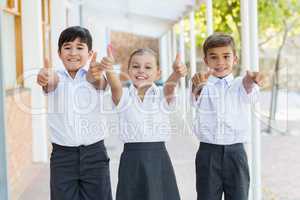 Smiling school kids showing thumbs up in corridor