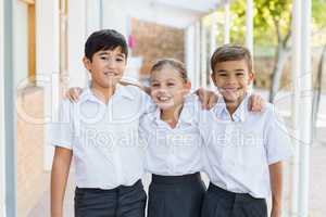 Smiling school kids standing with arm around in corridor