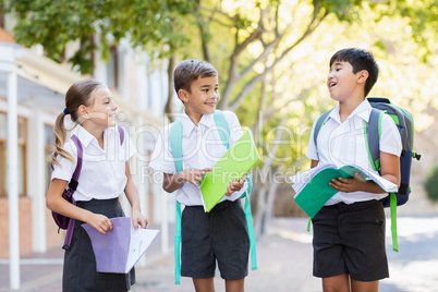 School kids talking to each other while reading books in campus