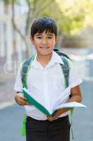 Happy schoolboy reading book in campus