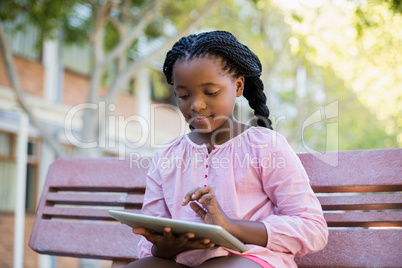 Schoolgirl sitting on bench and using digital tablet in campus