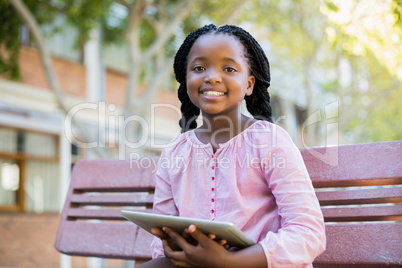 Happy schoolgirl sitting on bench with digital tablet