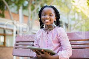 Happy schoolgirl sitting on bench with digital tablet