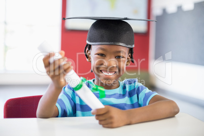 Schoolboy in mortar board holding certificate in classroom