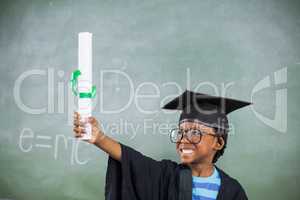 Excited schoolboy in mortar board holding certificate in classroom