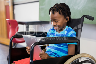 Schoolboy sitting on wheelchair and using digital tablet