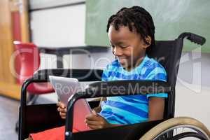 Schoolboy sitting on wheelchair and using digital tablet