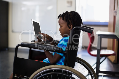 Schoolboy sitting on wheelchair and using digital tablet