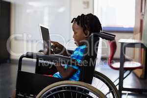 Schoolboy sitting on wheelchair and using digital tablet