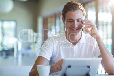 Smiling man talking on mobile phone while using digital tablet