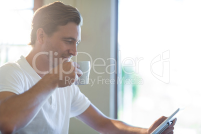 Man using digital tablet while having cup of coffee