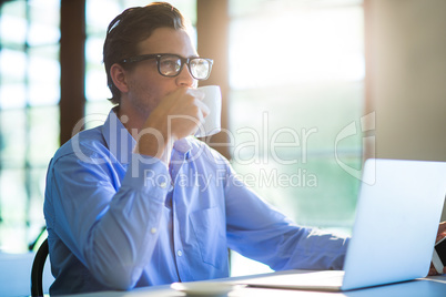 Man drinking a coffee while using a laptop