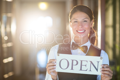 Portrait of smiling waitress holding open sign