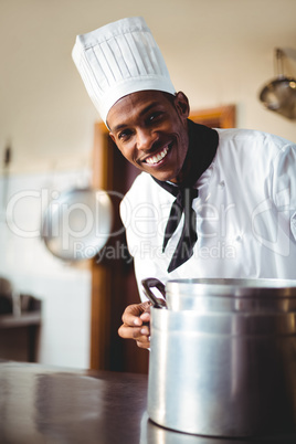 Smiling chef in kitchen holding cooking pot