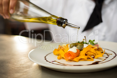 Chef pouring olive oil on meal