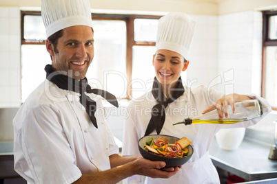 Happy chef pouring olive oil on salad