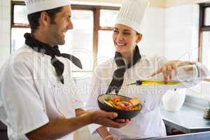 Happy chef pouring olive oil on salad