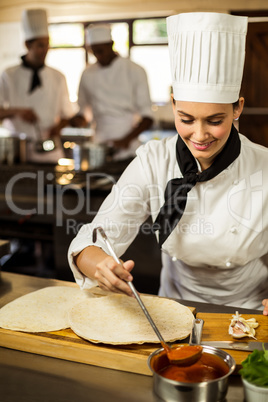 Head chef spreading sauce on a pizza