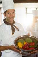 Portrait of smiling chef showing bowl of vegetable