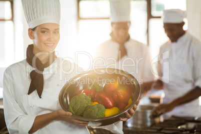 Portrait of smiling chef showing bowl of vegetable