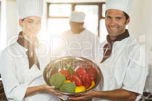 Portrait of two smiling chef holding a bowl of vegetable