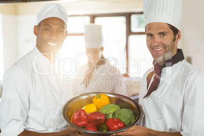 Portrait of two smiling chefs holding a bowl of vegetable