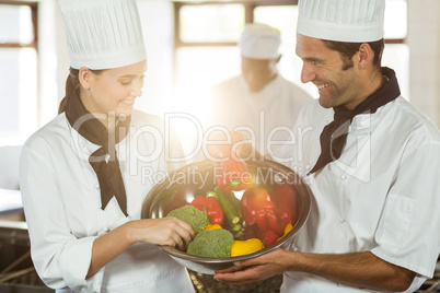Two smiling chefs holding a bowl of vegetable