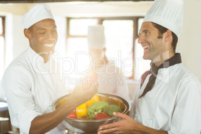 Two smiling chef holding a bowl of vegetable