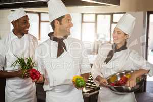 Smiling three chefs holding a vegetables