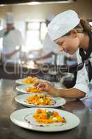 Female chef garnishing plate of food