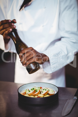 Mid section of chef sprinkling pepper on a salad