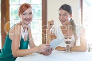 Two smiling women sitting in restaurant with a digital tablet