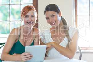 Two smiling women sitting in restaurant with a digital tablet