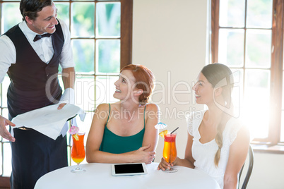 Waiter serving cocktail to women in restaurant