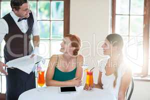 Waiter serving cocktail to women in restaurant