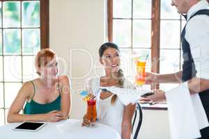 Waiter serving cocktail to women in restaurant