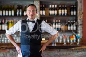 Portrait of confident waiter standing with hands on hip