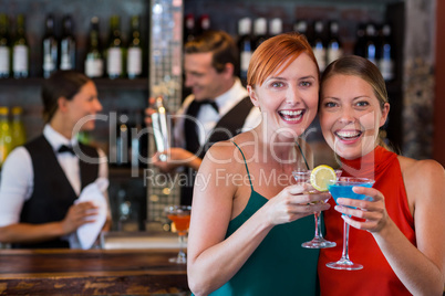 Portrait of friends holding a cocktail in front of bar counter