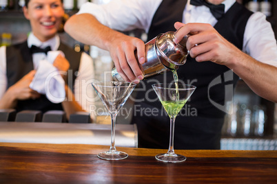 Mid section of bartender pouring cocktail into glasses