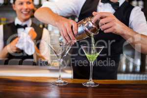 Mid section of bartender pouring cocktail into glasses