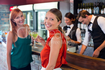 Portrait of friends holding a cocktail in front of bar counter